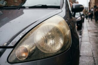 Phare avant jauni et oxydé d'une voiture compacte usagée garée dans une rue urbaine humide