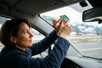 Femme collant la vignette autoroutière suisse 2026 sur le pare-brise d'une voiture